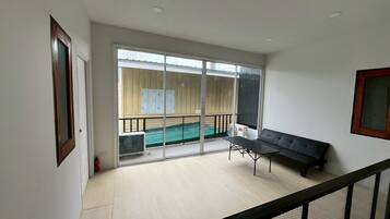 A room with a balcony, a sliding glass door, a black sofa, and a small table.