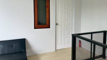 A room with a white door, a wooden-framed window, a black leather sofa, and a black metal railing.