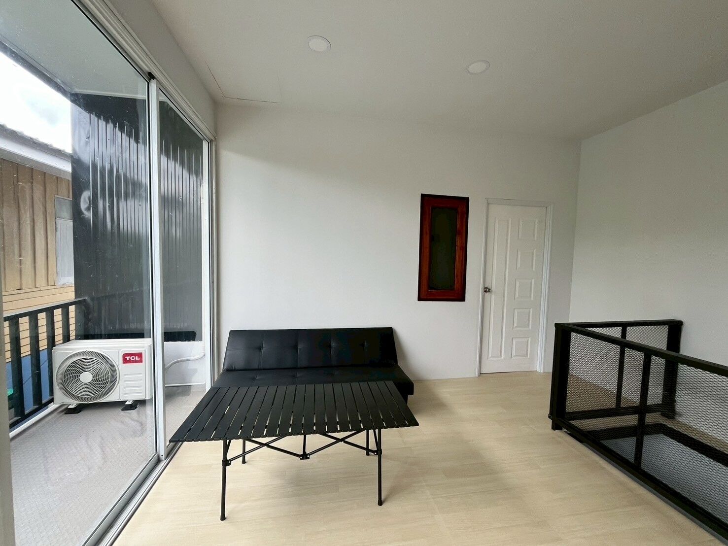 A balcony with a black table and chairs, a white door, and a window with a view of a building.