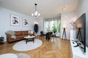 Una sala de estar moderna con un sofá de cuero marrón, una mesa de comedor con sillas, un televisor de pantalla plana y un ventanal con cortinas.