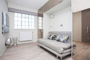 A modern room with a sofa, a radiator, a window, and a cabinet. - Tranquil Small Studio with AC in vibrant Chelsea (London)