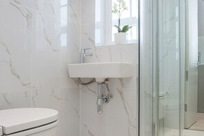 A bathroom with a white toilet, a sink, and a glass shower enclosure. - Tranquil Small Studio with AC in vibrant Chelsea (London)