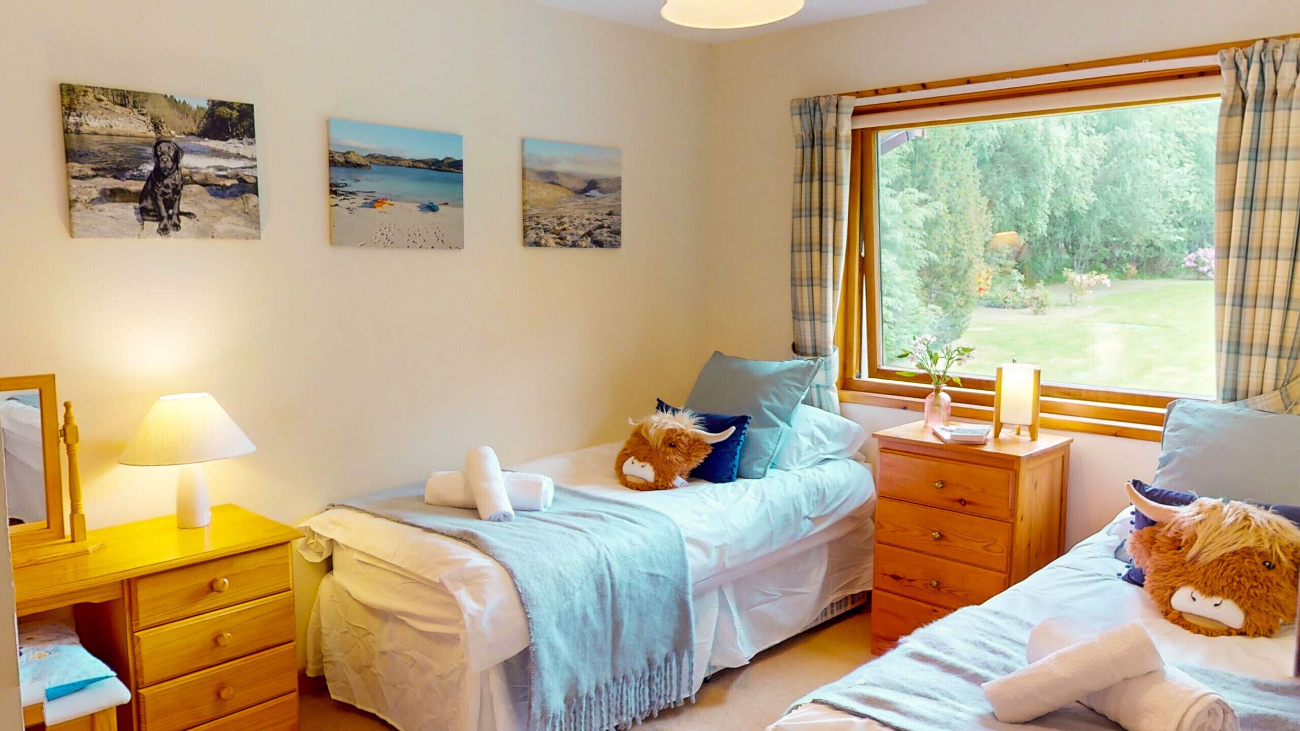 Une chambre avec deux lits, une table de chevet, une commode et une fenêtre donnant sur un paysage verdoyant.