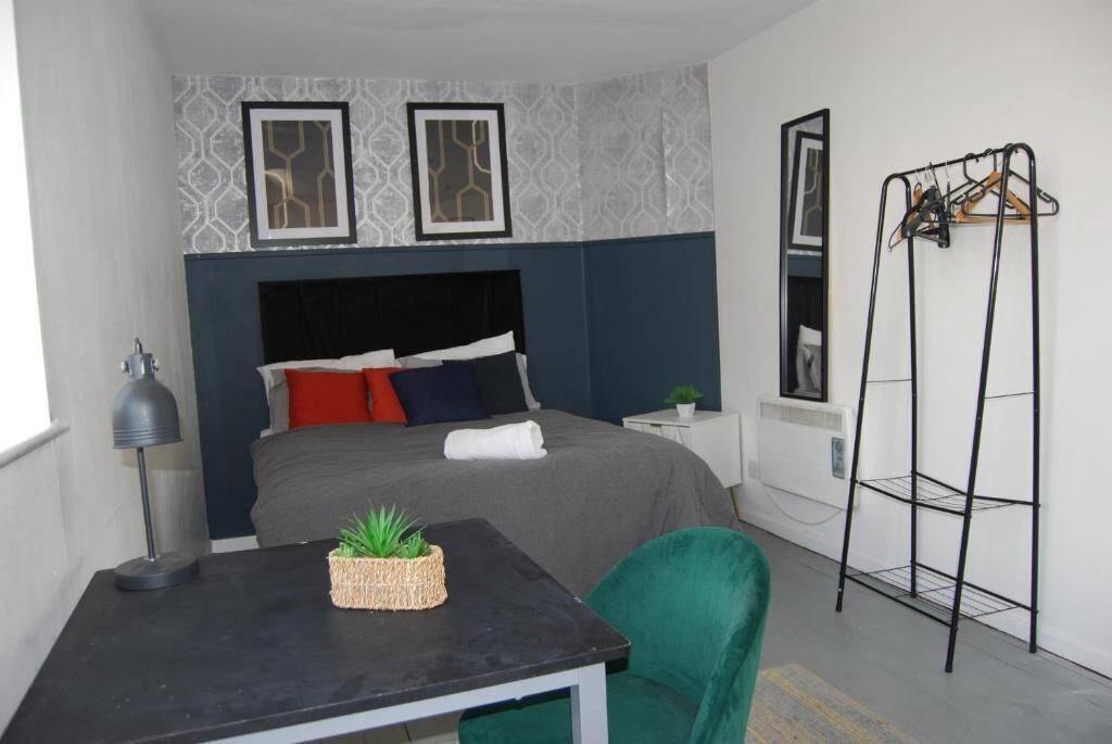 A bedroom with a bed, bedside table, lamp, chair, and a wall-mounted shelf.