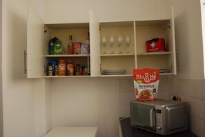 Eine Küche mit offenen Schränken, in denen Lebensmittel, eine Mikrowelle und eine Packung Bio & Me Granola stehen.