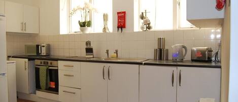 A kitchen with white cabinets, a microwave, a kettle, and a window with a plant.