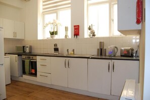 Eine Küche mit weißen Schränken, einer Mikrowelle, einem Wasserkocher und einem Fenster mit einer Pflanze.