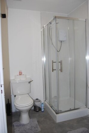 A bathroom with a toilet, a glass-enclosed shower, and a small trash bin. - Leicester Central Stay Near LRI and Uni (Leicester)