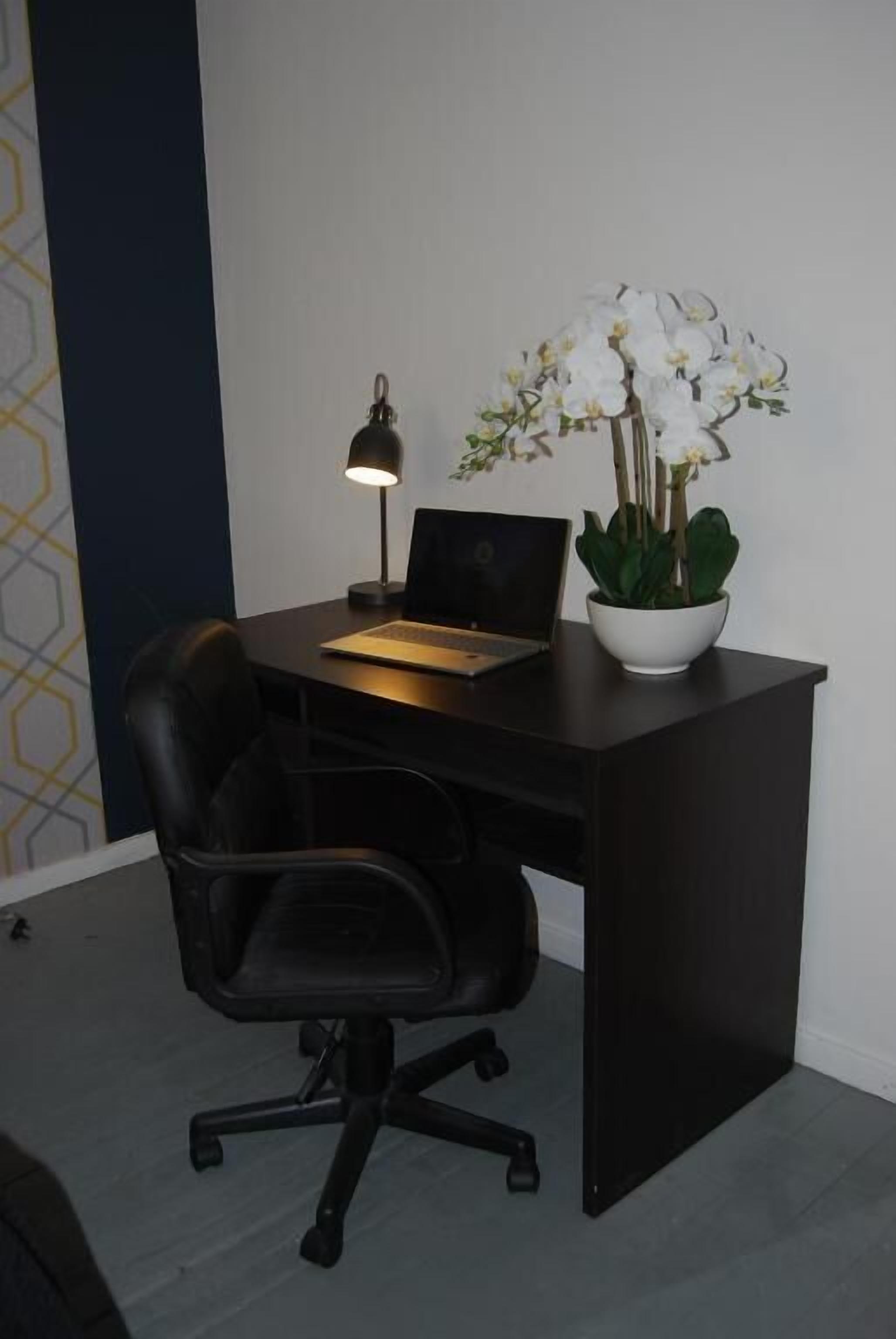 A dark wooden desk with a laptop, a desk lamp, and a potted orchid.