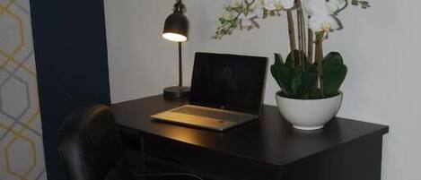 A dark wooden desk with a laptop, a desk lamp, and a potted orchid.