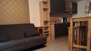 Un soggiorno con un divano, un angolo cottura con mobili e un pavimento piastrellato.