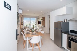 Una cocina moderna con refrigerador de acero inoxidable, horno empotrado y comedor con mesa de madera y sillas blancas.