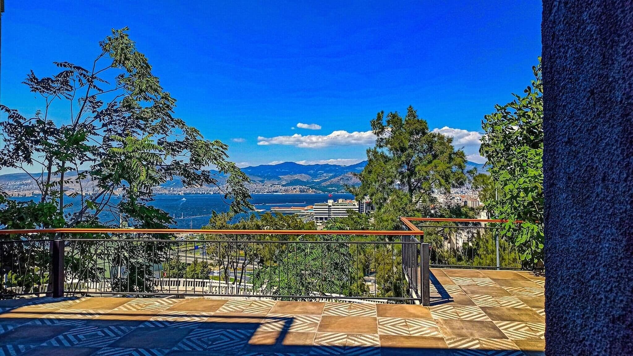 Un balcone con pavimento decorato, ringhiera e vista sulla città costiera con montagne sullo sfondo.