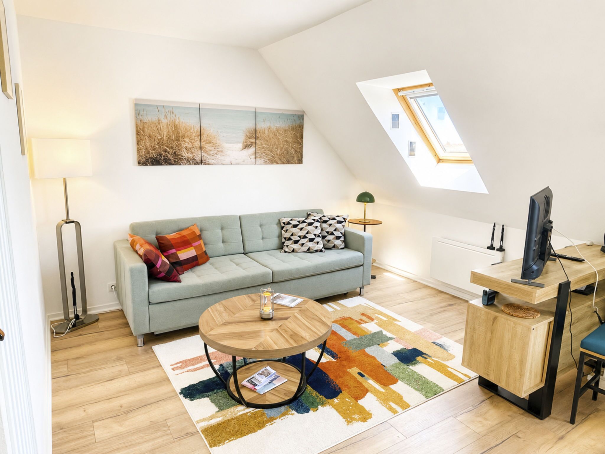 Ett modernt vardagsrum med en soffa, ett runt soffbord, ett TV-bord och ett takfönster.