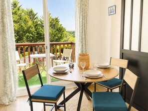 Un coin repas avec une table dressée pour deux personnes, des chaises et une vue sur l’extérieur.