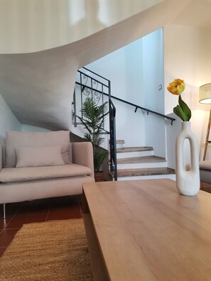 A modern living room with a sofa, a wooden coffee table, a potted plant, and a staircase with a railing.
