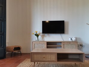 Una sala de estar moderna con un televisor de pantalla plana montado en la pared, una mesa consola de madera con un florero, un sillón de mimbre y una mesa de centro grande.