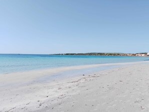 Una playa con aguas azules cristalinas, una orilla arenosa y una costa distante con edificios.