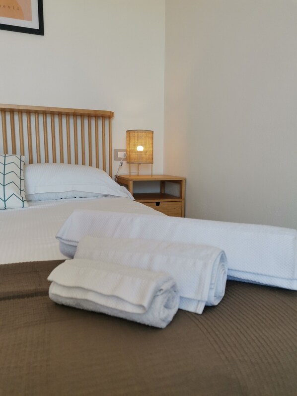 A neatly made bed with white linens, a bedside lamp, and a wooden nightstand.