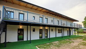 Un edificio de dos pisos con balcón, paseo techado y césped artificial verde.