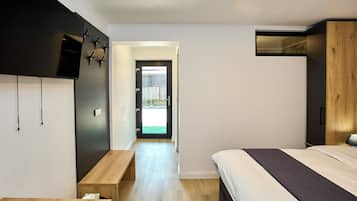 Un dormitorio moderno con cama, una banca, un televisor y una puerta que da a un espacio exterior.