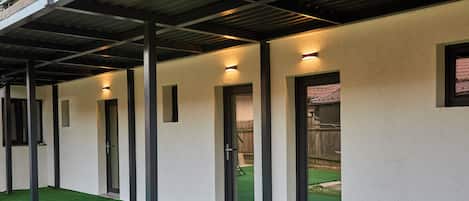 A corridor with doors, a covered area with artificial grass, and a metal roof structure.