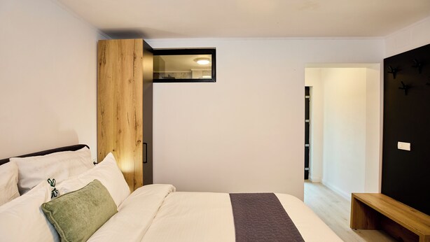 Un dormitorio moderno con cama, mesitas de noche, cabecero de madera y un ventanal pequeño.