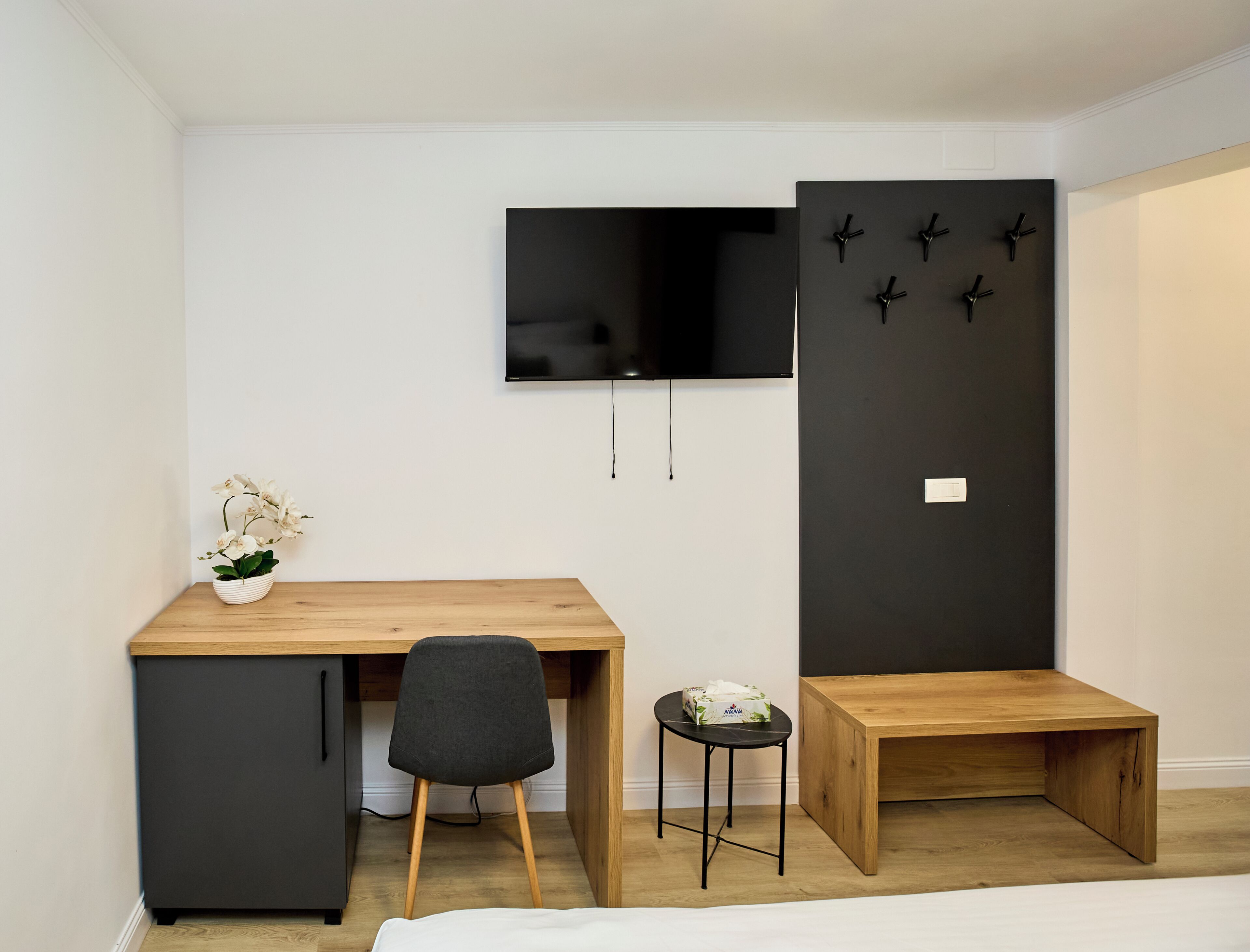 A bedroom with a bed, a desk with a chair, a small table, a TV, and a wardrobe.