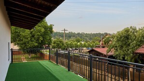 Un balcón con césped artificial verde, baranda metálica y vista a una zona residencial con árboles y casas.