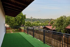 A balcony with artificial green turf, a metal railing, and a view of a residential area with trees and houses.