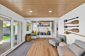 Un interior moderno con techo de madera, una zona de estar con sofá gris, un banco empotrado con espacio de almacenamiento y una pared decorada con tablas de remo.