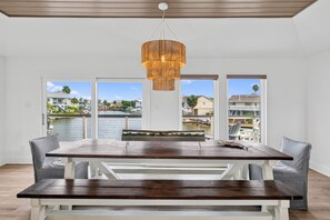 A dining area with a wooden table and benches, a hanging light fixture, and large windows with a view of a waterfront. - Waterfront Canal Home w/ Private Dock |Sleeps 11 (Rockport)