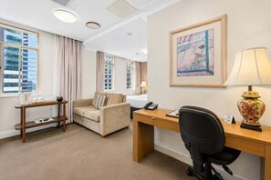 Een hotelkamer met een bed, bureau, stoel, bijzettafeltje, lamp en een schilderij aan de muur.