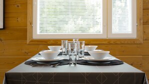 A dining table set with white bowls, glasses, and cutlery, positioned in front of a window with blinds. - Apartment A 3 Talja, Private Sauna By Lapland Host (Rovaniemi)