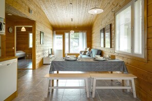 Interior de una cabaña de madera con mesa de comedor, bancos, sofá y zona de cocina.