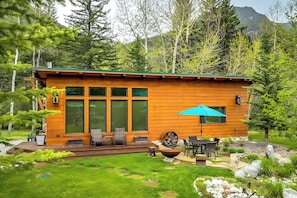 Une cabane en bois dotée de grandes fenêtres, d’un espace extérieur aménagé et d’un foyer.