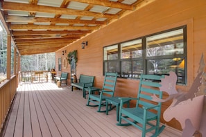 Una terraza de madera con mecedoras y una mesa, ventanas amplias y techo de madera.
