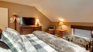 Quarto com cama, televisão, duas luminárias, uma cadeira e um banco.