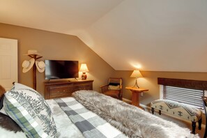 Un dormitorio con una cama, televisión, dos lámparas, una silla y un banco.