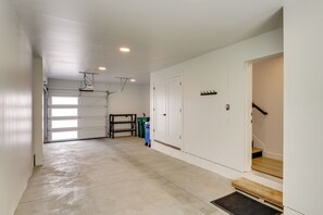 Ett rent och väl upplyst garage med ett betonggolv, en arbetsbänk i metall och en grön soptunna.