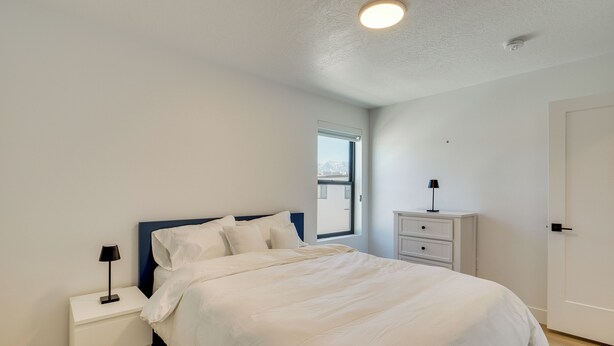 A bedroom with a bed, a nightstand, a dresser, and a window with a view. - Brand-New Townhome Near Dtwn Salt Lake & Trails! (Millcreek)