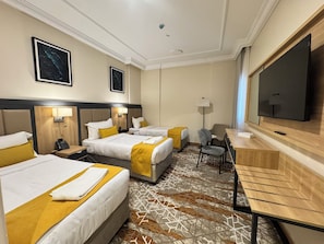 Une chambre d’hôtel avec deux lits, un bureau, une chaise, un téléviseur à écran plat et un tapis à motifs.