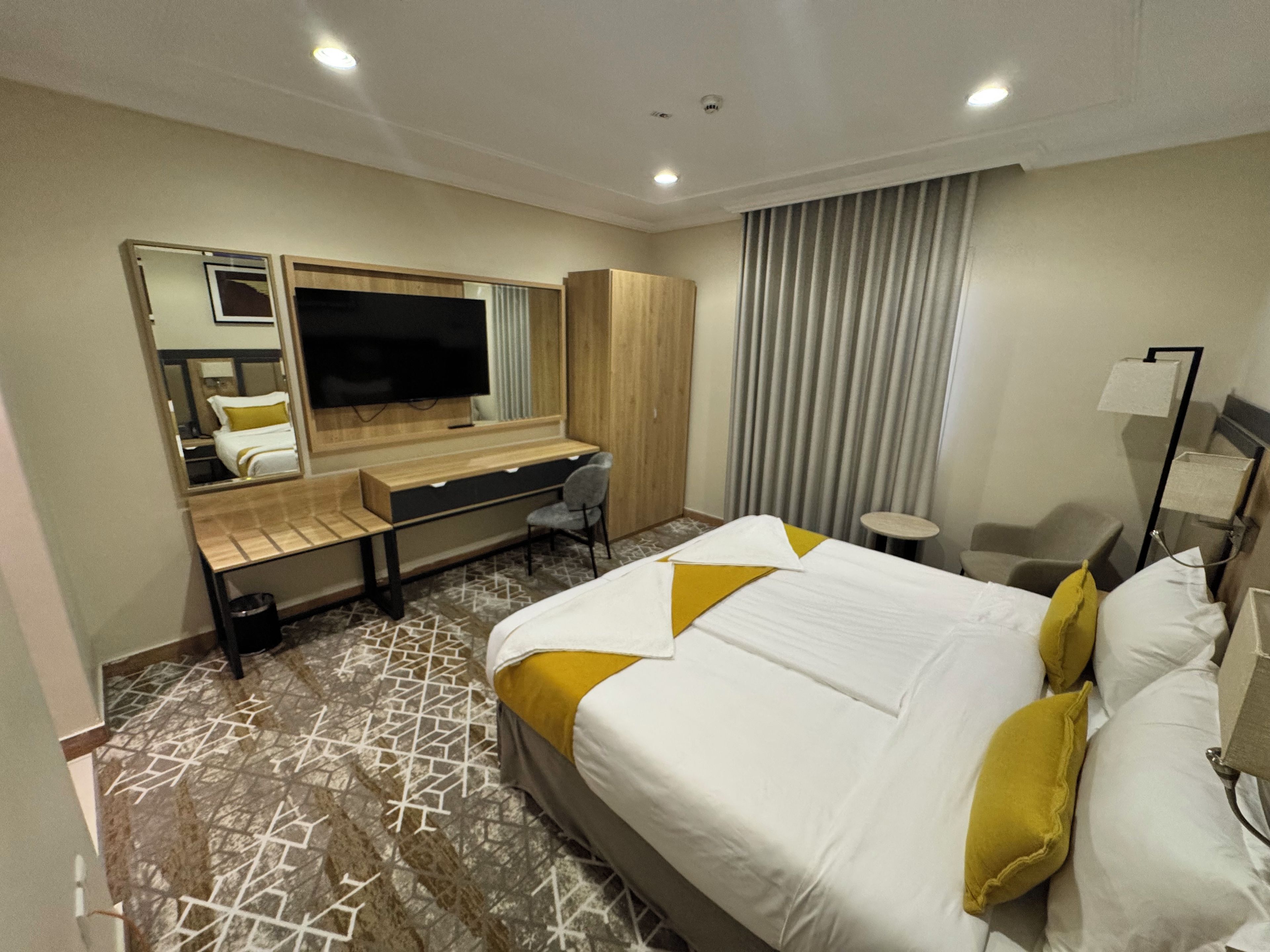 Ein Hotelzimmer mit Bett, Schreibtisch, Stuhl, Fernseher und Kleiderschrank.