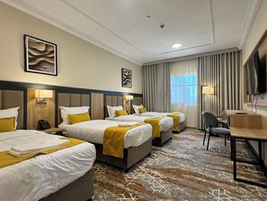 Une chambre d’hôtel avec trois lits, un bureau, une chaise, une télévision et des œuvres d  ’art accrochées aux murs.