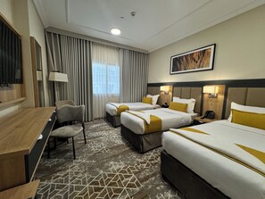 Une chambre d’hôtel avec deux lits, un bureau, une chaise, une télévision et une fenêtre avec des rideaux.