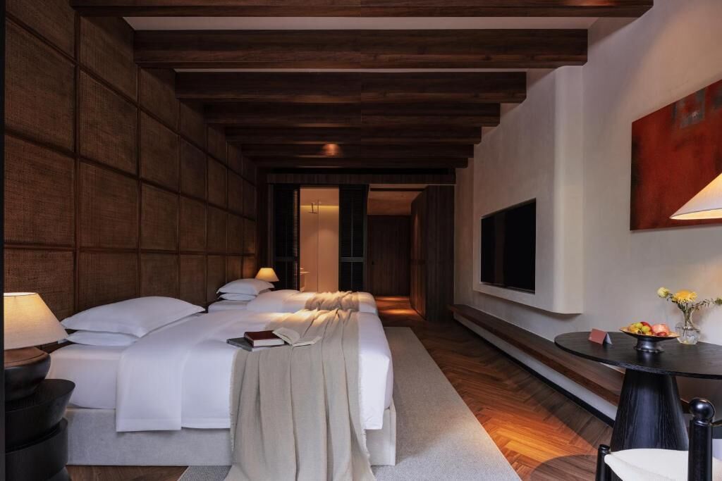 Habitación de hotel con una cama grande, un televisor, una mesita con flores y techo de madera.
