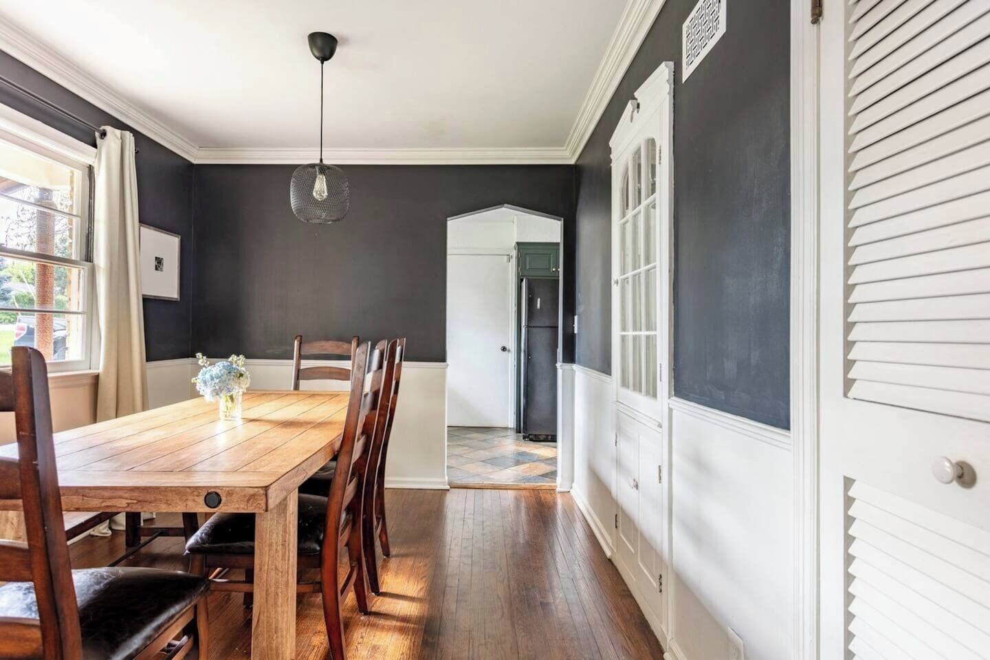 Un coin repas avec une table et des chaises en bois, un luminaire suspendu et une vue sur la cuisine.