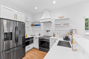 A modern kitchen with stainless steel appliances, white cabinetry, and a central island with a sink and countertop. - Private Pool + Firepit + Beach Gear | Short Drive to Beach + Las Olas | Al Mare (Fort Lauderdale)