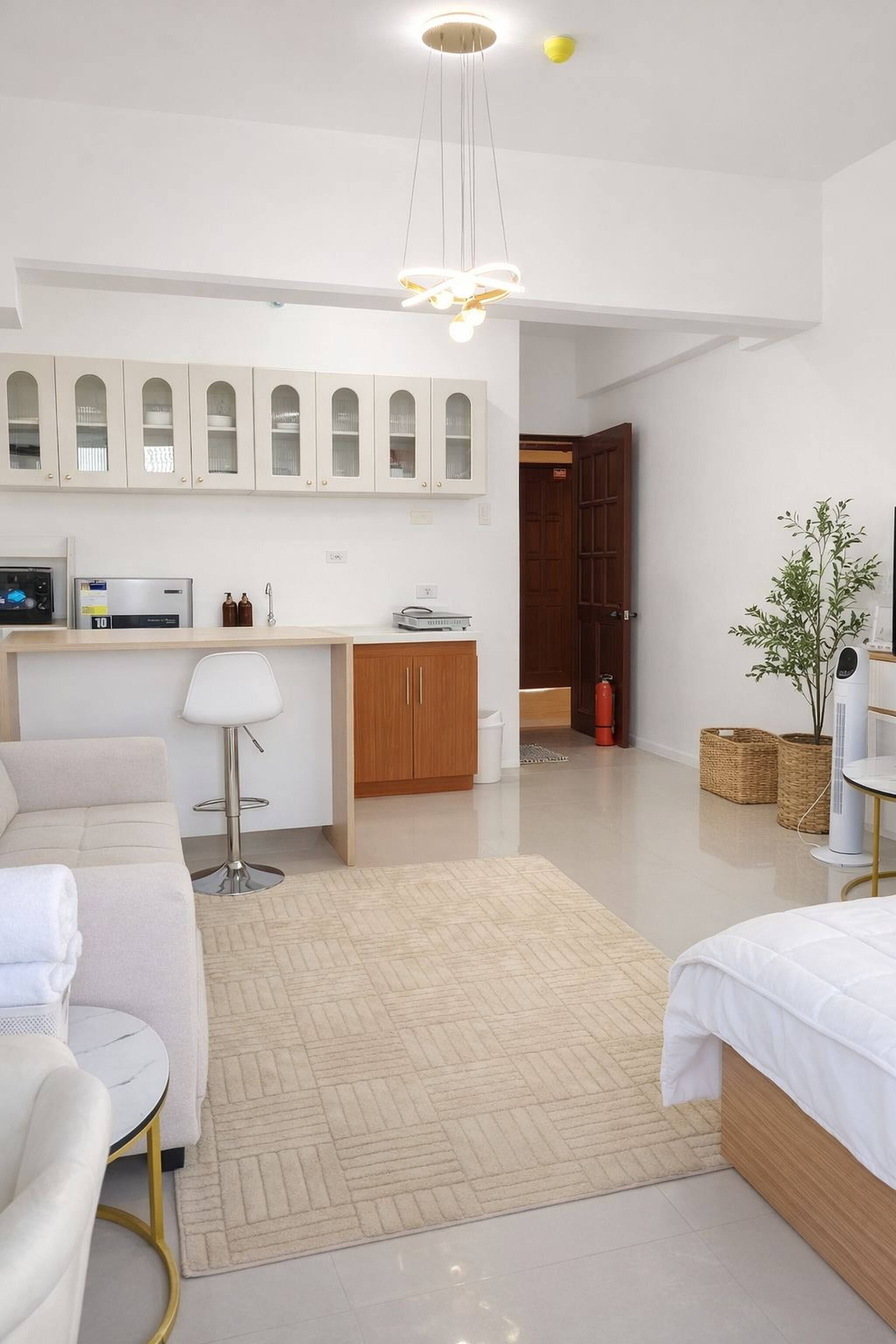 Una habitación moderna y bien iluminada con kitchenette, un sofá, una mesita y una planta en maceta.