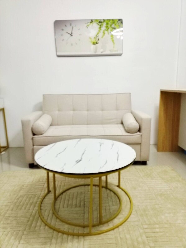 Una stanza con un divano beige, un tavolino con cornice dorata e una sveglia a muro.